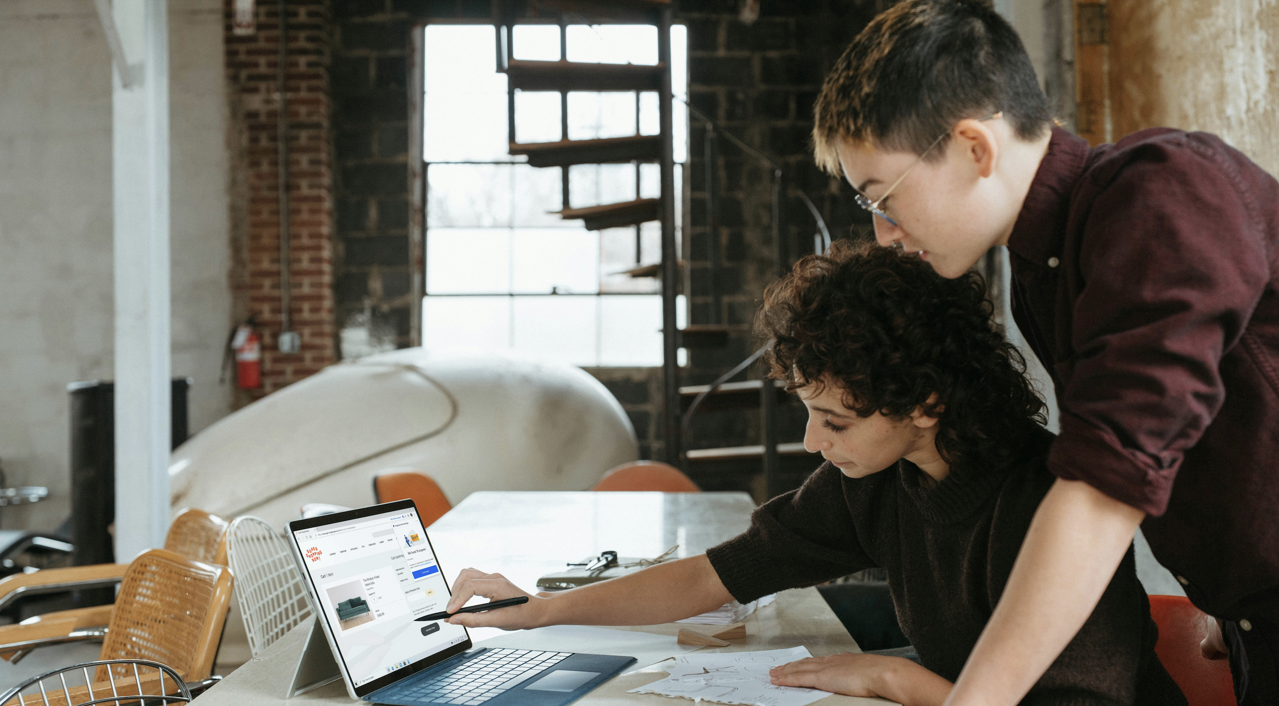 Two business team members collaborating on a design project using a laptop in a modern workspace.